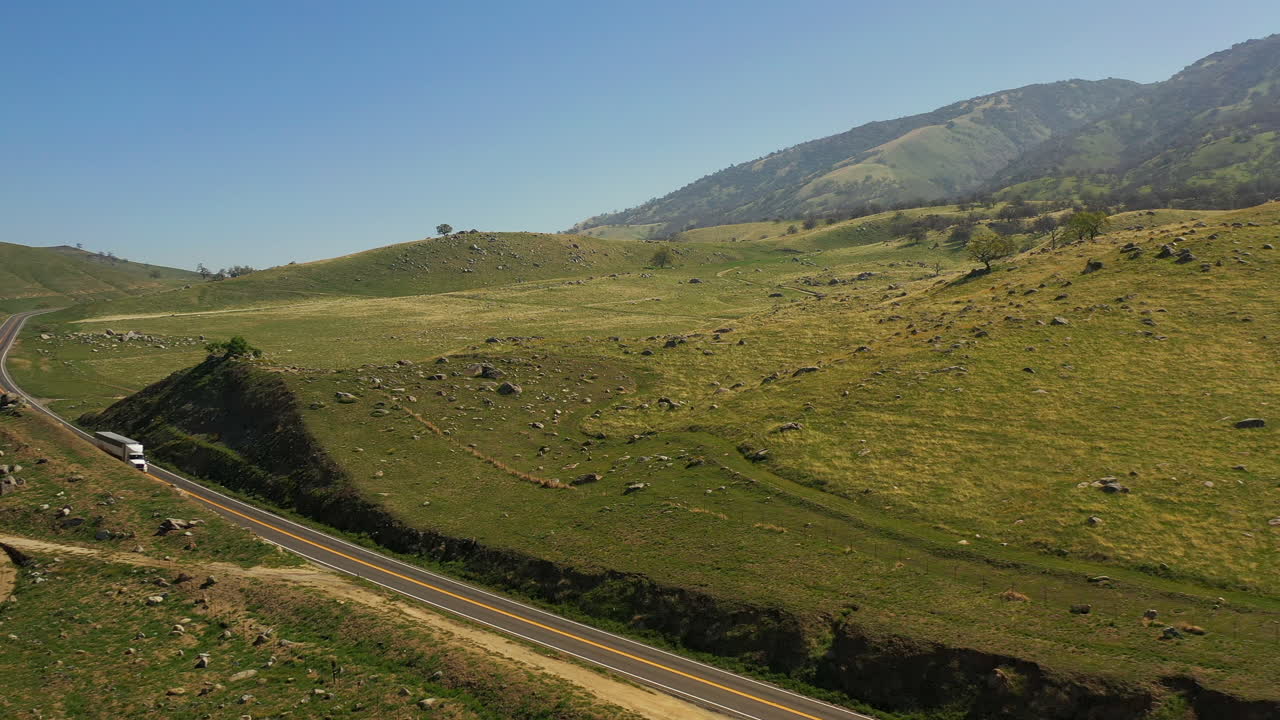 In primavera, mentre l'erba è verde, un camion percorre un'autostrada nella California del Sud - vista aerea.