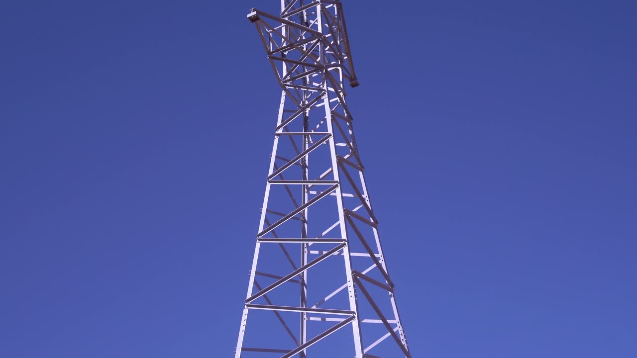 torre eléctrica de alto voltaje en un paisaje montañoso contra un cielo azul claro, revelando el movimiento de la cámara de inclinación, vista panorámica