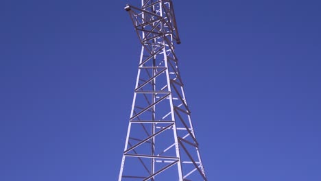 Torre-Eléctrica-De-Alta-Tensión-En-Un-Paisaje-Montañoso-Contra-Un-Cielo-Azul-Claro,-Revelando-El-Movimiento-De-La-Cámara-Inclinada,-Vista-Panorámica
