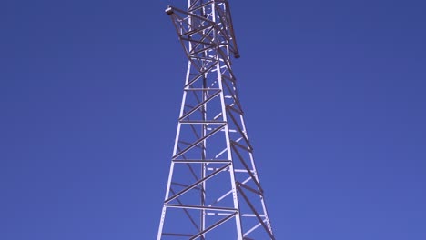 torre eléctrica de alto voltaje en un paisaje montañoso contra un cielo azul claro, revelando el movimiento de la cámara de inclinación, vista panorámica
