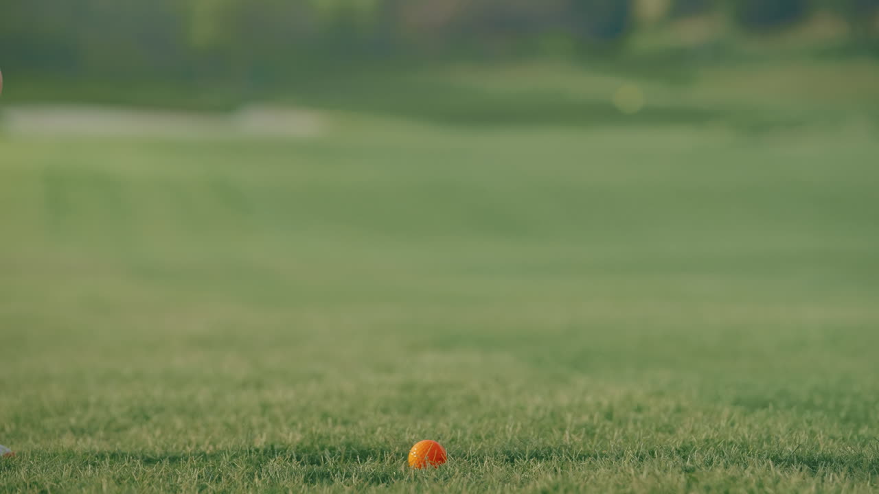 A slow motion close-up shows an iron making crisp contact with an orange ball on the fairway, sending a divot flying. The clip highlights precision, power, and the textures of the course surface.