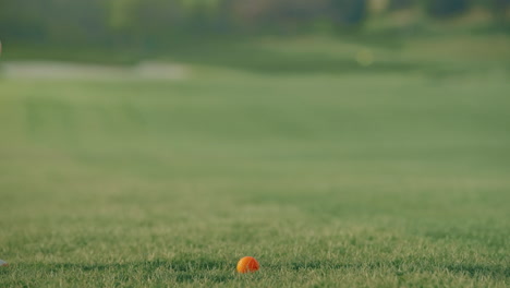 a slow motion close-up shows an iron making crisp contact with an orange ball on the fairway, sending a divot flying. the clip highlights precision, power, and the textures of the course surface.