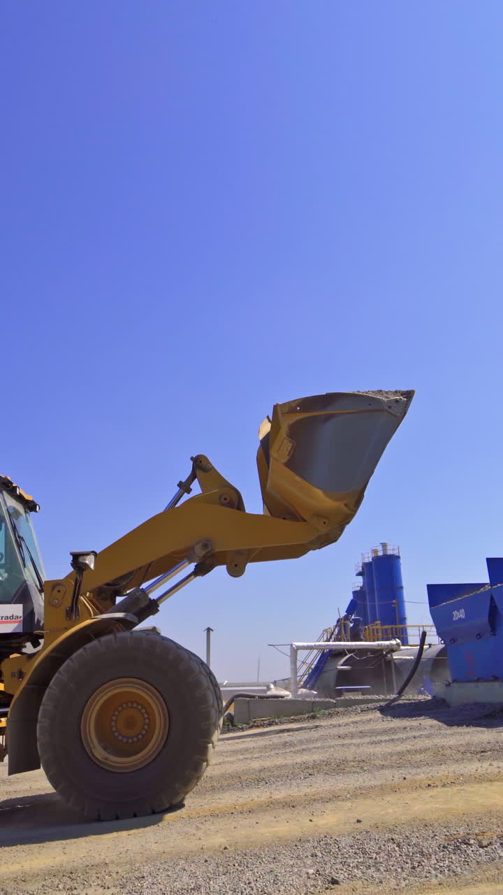 Contemporary asphalt factory background. Excavator transports asphalt into special tanks outdoors. Vertical video