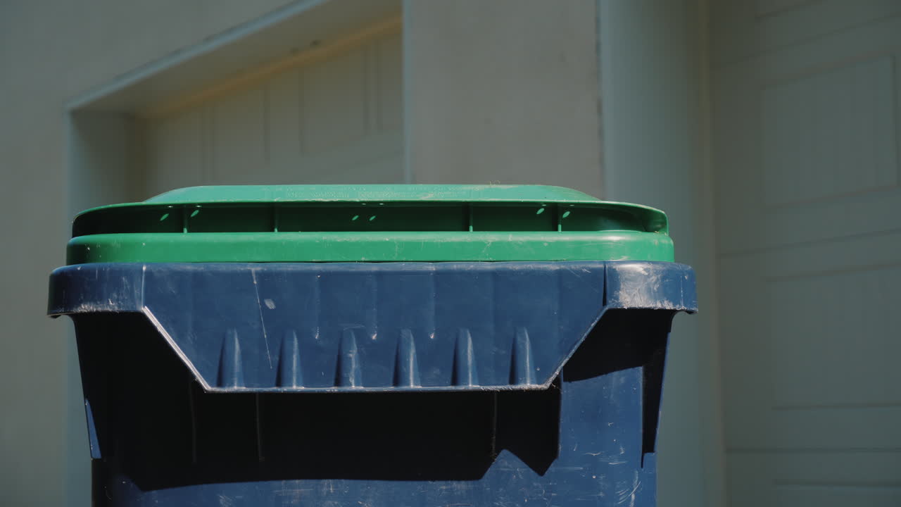 A Man Throws A Garbage Bag Into A Waste Tank Near His House