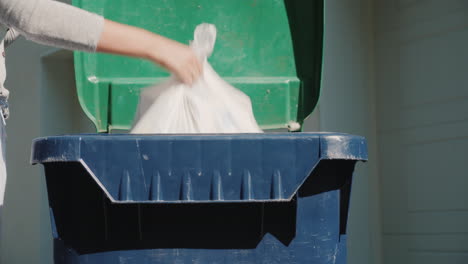 un hombre arroja una bolsa de basura a un tanque de desechos cerca de su casa