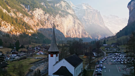 Drone-pushes-past-homes-and-chapel-in-shaded-valley-of-Lauterbrunnen,-Switzerland