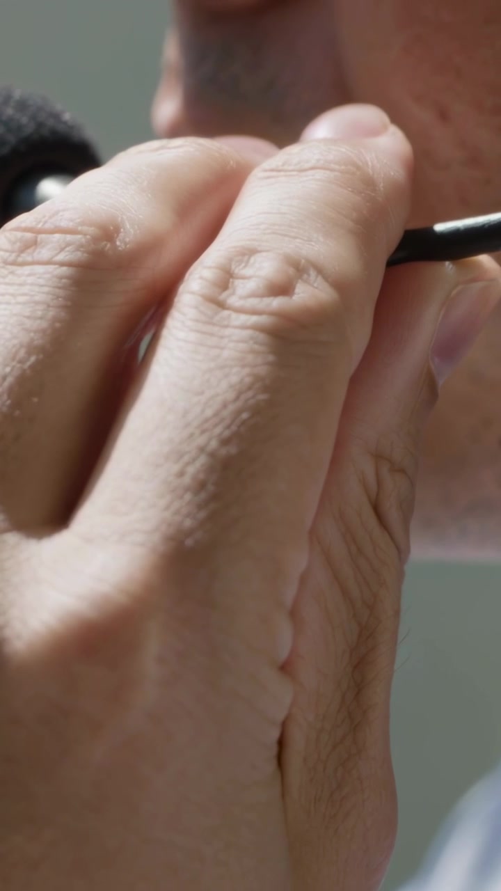 Vertical video: Bringing right hand, man holding wired microphone in close-up near mouth, speaking