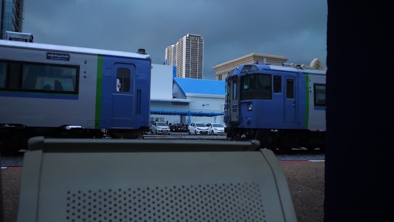 Trains at Phnom Penh city railway station under dark sky, viewed from platform seat