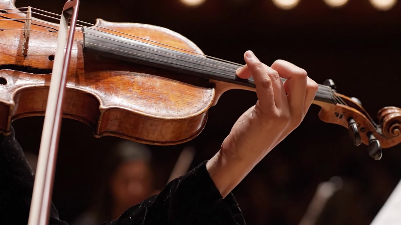 Esibizione Coinvolgente: Un Primo Piano della Mano di un Violinista che Impugna l'Archetto e Suona Abilmente il Violino in un'Emozionante Ambientazione di Concerto Musicale
