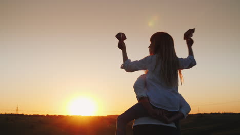 the girl is sitting on her mother's shoulders playing with paper airplanes a happy family 4k video