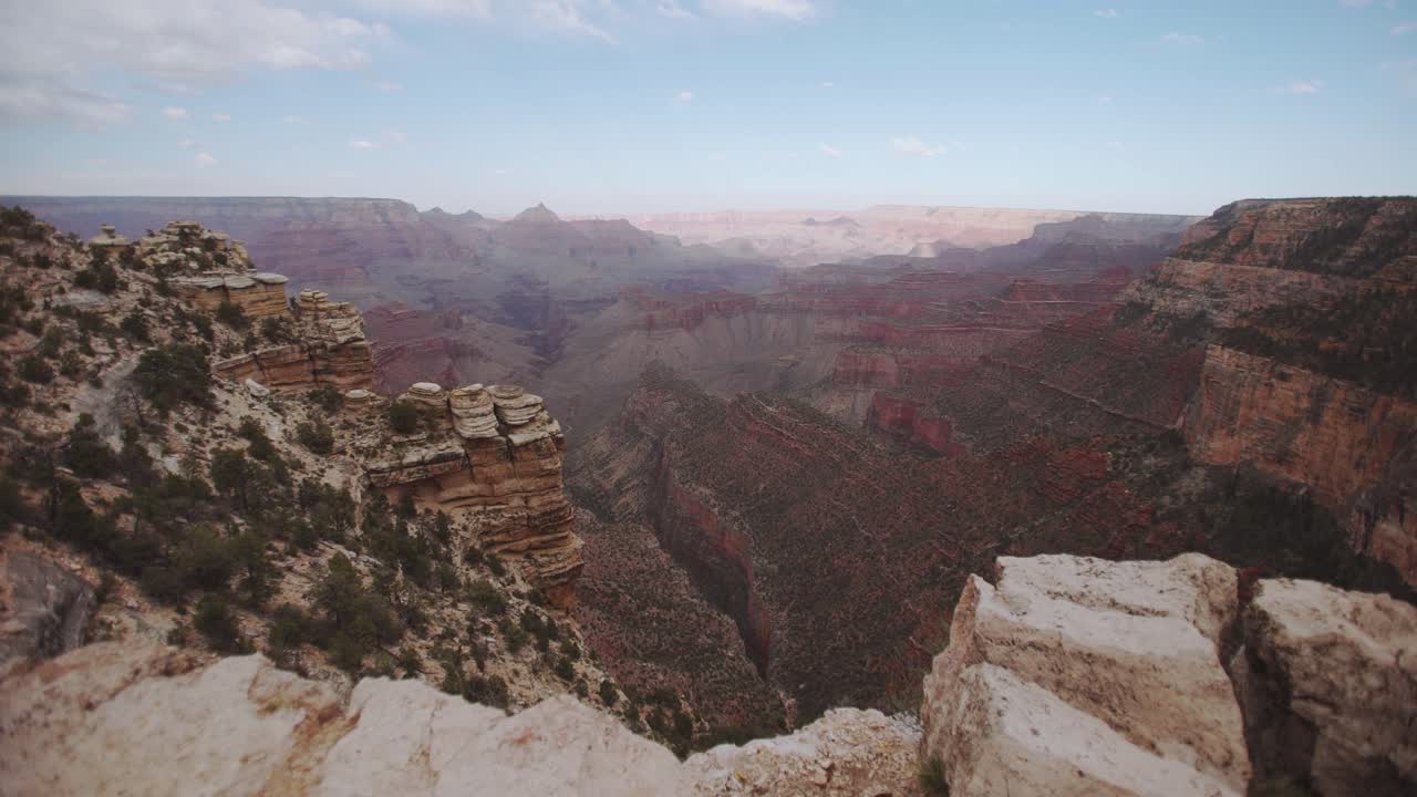 Grand Canyons klippekant, gimbal-bevægelse fremad afslører dalen nedenfor, med blå himmel, skydække, blød middagssol, røde klipper og skygger på canyonvæggene - Arizona USA