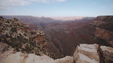 grand canyon cliff edge gimbal push forwards reveals valley below, with blue skies, cloud cover, soft midday sun, red rocks, and shadows on the canyon walls - arizona usa