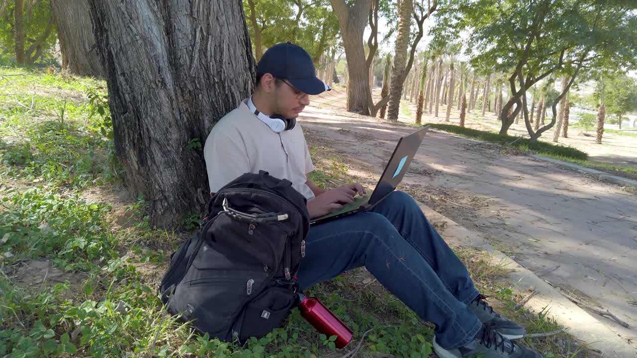 A man is sitting on the ground with a laptop and a backpack