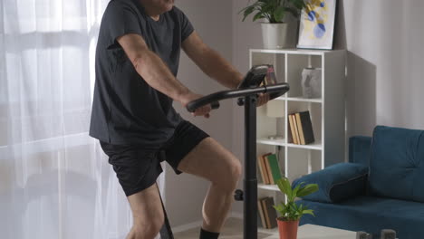 middle aged person is using modern exercise bike for training at home spinning pedals in his apartment at weekend keeping fit and health