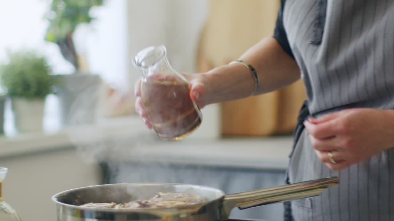 mujer vertiendo vino blanco para cocer la carne en la sartén