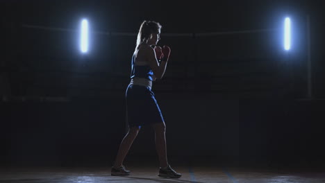 Boxer-woman-in-red-bandages-on-the-hands-of-and-blue-t-shirt-conducts-battle-with-of-practicing-the-speed-and-technique-strikes-hands.-Camera-movement-side-View.-Steadicam-shot