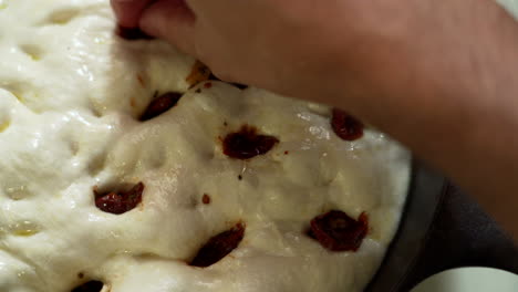 italian focaccia being made in a cast iron pan, pressing sundried tomatoes into it