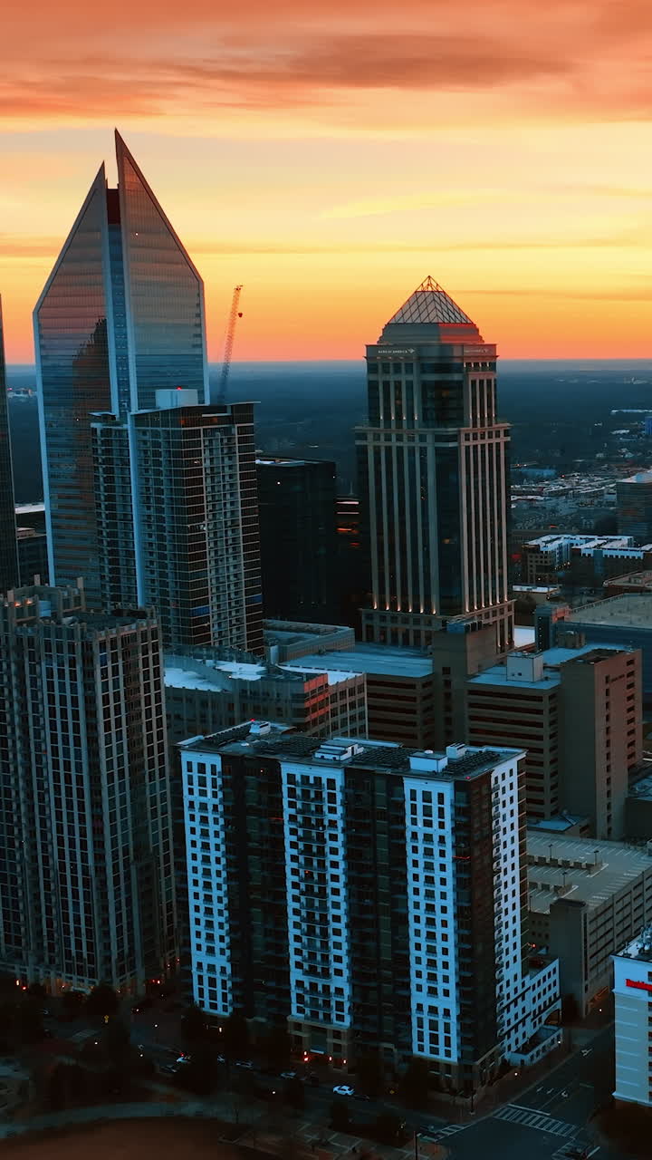 Stunning orange sky above the scenery of American metropolis. Group of skyscrapers and Bank of America Stadium in Charlotte, North Carolina, USA. Top view. Vertical video