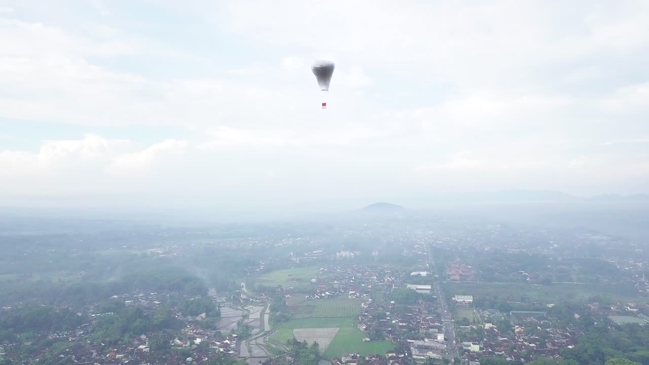 시골 산간 풍경에서 구름 사이를 날고 있는 인도네시아 국기가 달린 인도네시아 전통 풍선의 공중 추적 샷