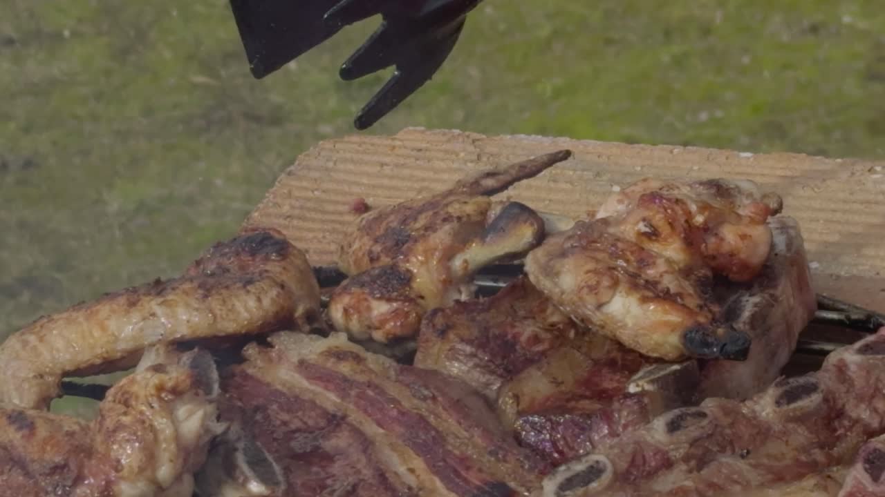 Kuře a hovězí maso otáčené kuchyňskými kleštěmi při grilování na grilu.