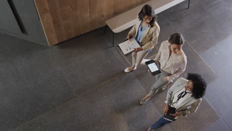 diverse female colleagues in discussion using tablet in office foyer, slow motion