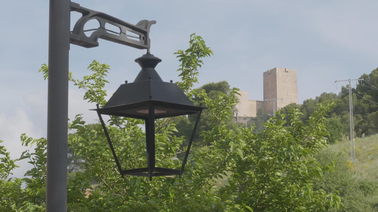Castillo de Santa Catalina, situado en la cima de una colina en Jaén (España), enmarcado por una clásica farola de hierro negro y exuberantes árboles verdes en primer plano