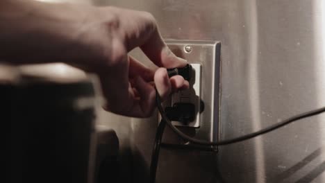 a person plugging in an electrical kitchen appliance to a two gang socket with another appliance plugged in - closeup shot