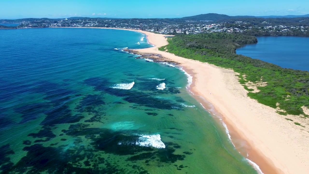 Luftfoto fra drone af havbølger, der bryder mod et klipperev, fantastisk sandstrandskystlinje med Wamberal-lagunen, Central Coast Australien, surfingparadis, turisme.