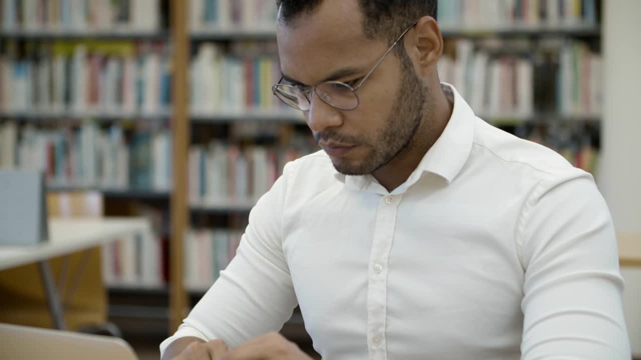 profesor afroamericano enfocado escribiendo en una laptop en la biblioteca