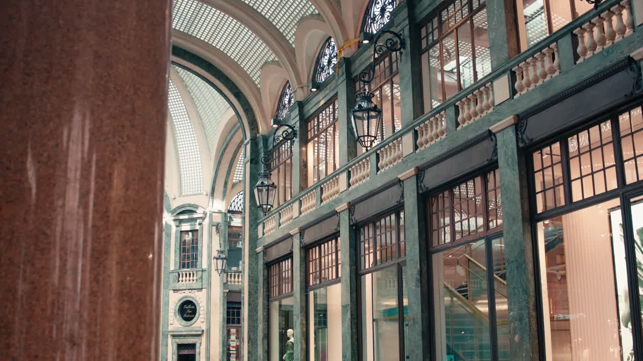 Foto interni dal basso angolo della Galleria Subalpina a Torino che mostra colonne verdi decorate, ampie finestre e dettagli architettonici classici dello storico passaggio commerciale coperto