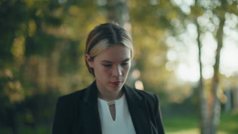professional woman enjoys coffee in tranquil park setting with trees behind her as warm sunlight filters through leaves, casting soft natural light across her focused face during outdoor break