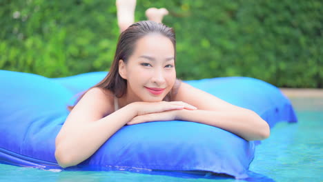 Retrato-De-Hermosa-Mujer-Exótica-Sexy-En-Un-Colchón-De-Aire-En-La-Piscina-En-Vacaciones-Tropicales,-Mirando-A-La-Cámara