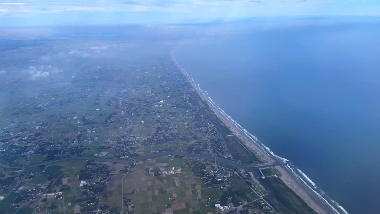 Coastline and farmland stretching across a wide landscape beneath a cloudy sky, aerial view