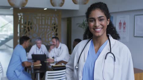 Portrait-of-asian-female-doctor-smiling,-with-colleagues-in-discussion-in-background