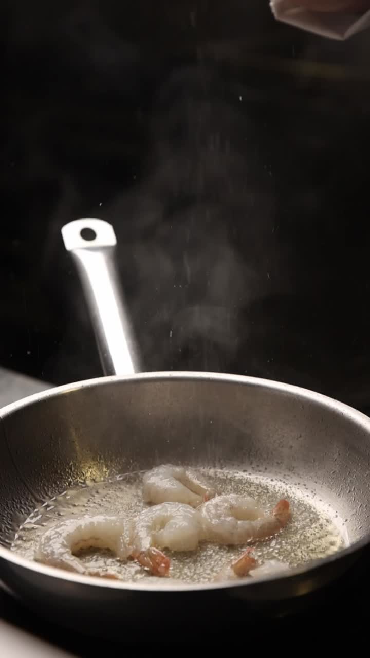 Chef che condisce i gamberi che friggono in una padella calda