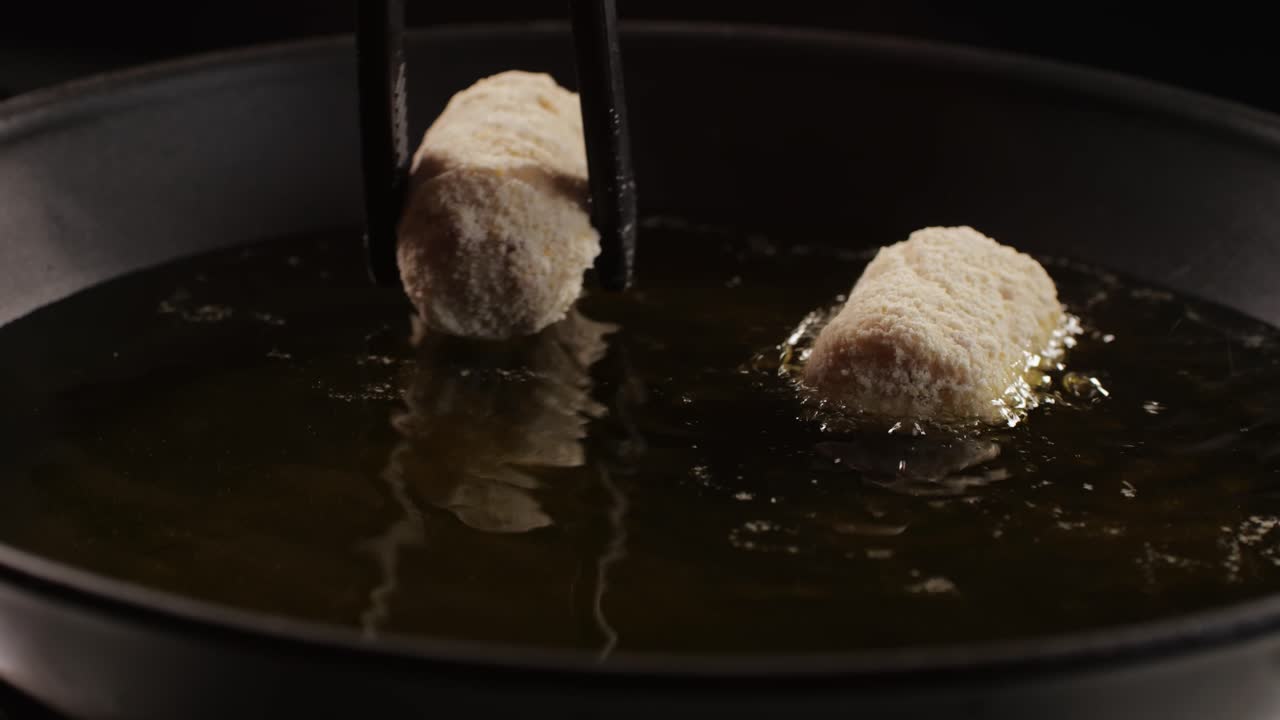 Portuguese croquettes broiling on black frying pan close-up macro. Breaded croquette of fish, potatoes and ham. Man cooking spanish food. High quality 4k footage