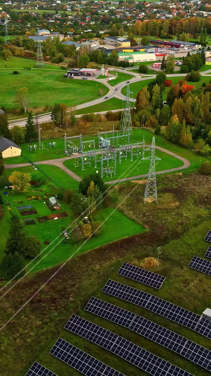 Rows of solar panels and an electrical substation in a rural landscape with green fields and trees