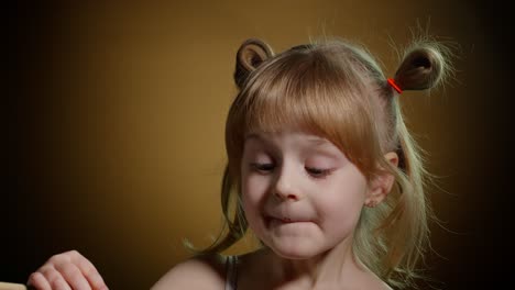 joyful smiling child kid girl with dirty face from melted chocolate on dark background in studio