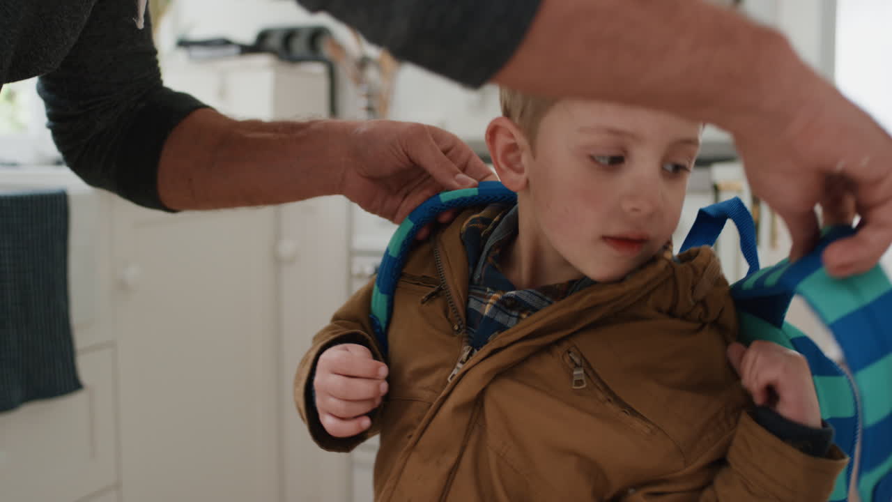 아버지는 아들을 학교로 준비시키고 아버지는 작은 소년에게 머리에 키스를 하고 작별 인사를 하고 있습니다.