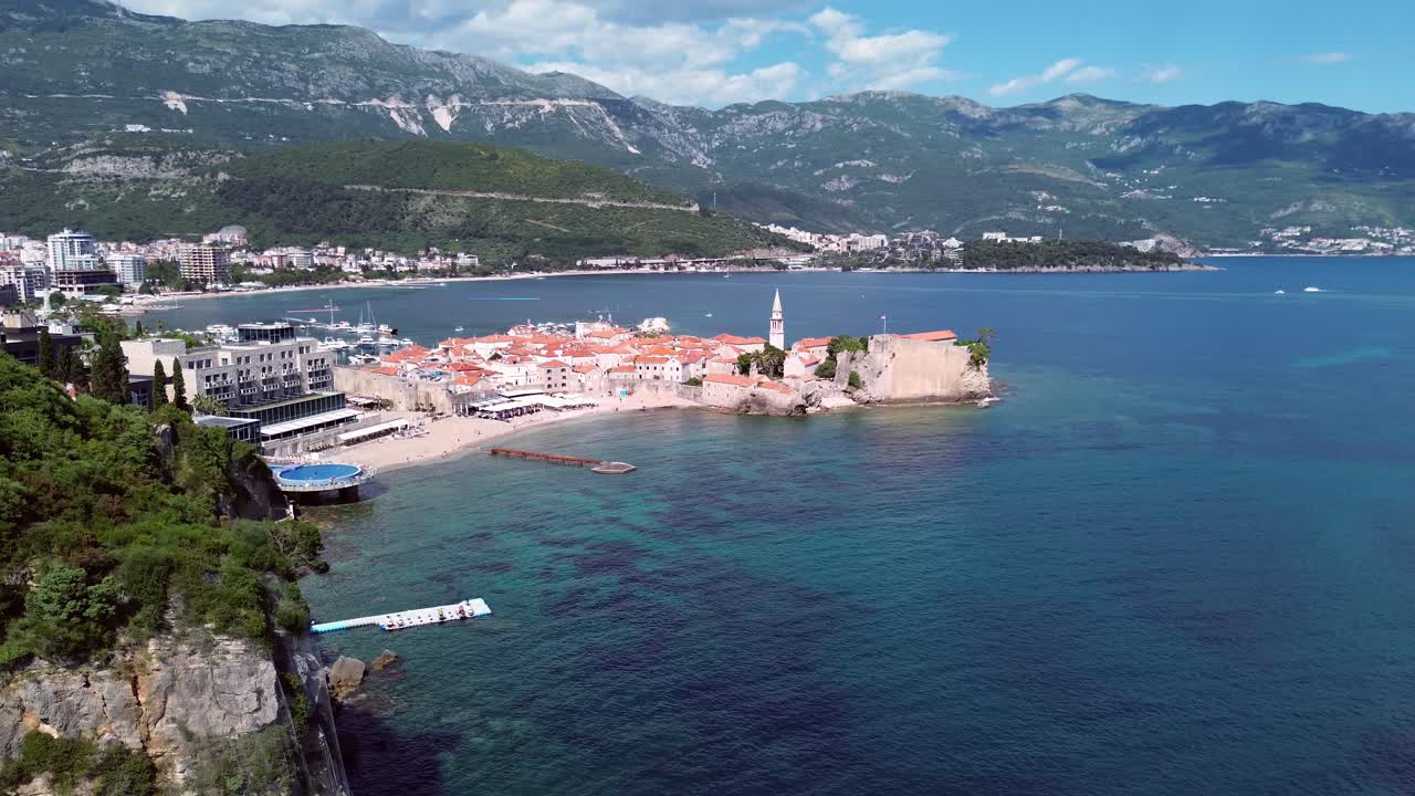 Medieval fortress in old town of Budva on Adriatic coast with mountains in backdrop, Revealing drone shot, Panorama