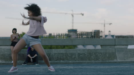 Mujer-Bailando-Atractiva-Joven-Bailarina-De-Raza-Mixta-Realizando-Baile-Callejero-De-Estilo-Urbano-En-La-Ciudad-Practicando-Movimientos-De-Estilo-Libre-Amigos-Viendo-Disfrutando-Pasar-El-Rato-Al-Atardecer