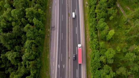 Tilt-up-drone-shot-of-2-lane-highway-built-between-tall-trees-and-green-belt-in-European-country-with-nice-traffic-flow-cars-and-trucks