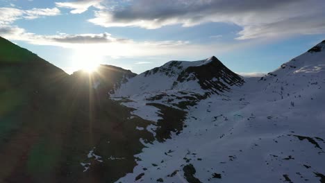 drone riser reveals sunrise sun rays bursting over mountains, snowy italian alps