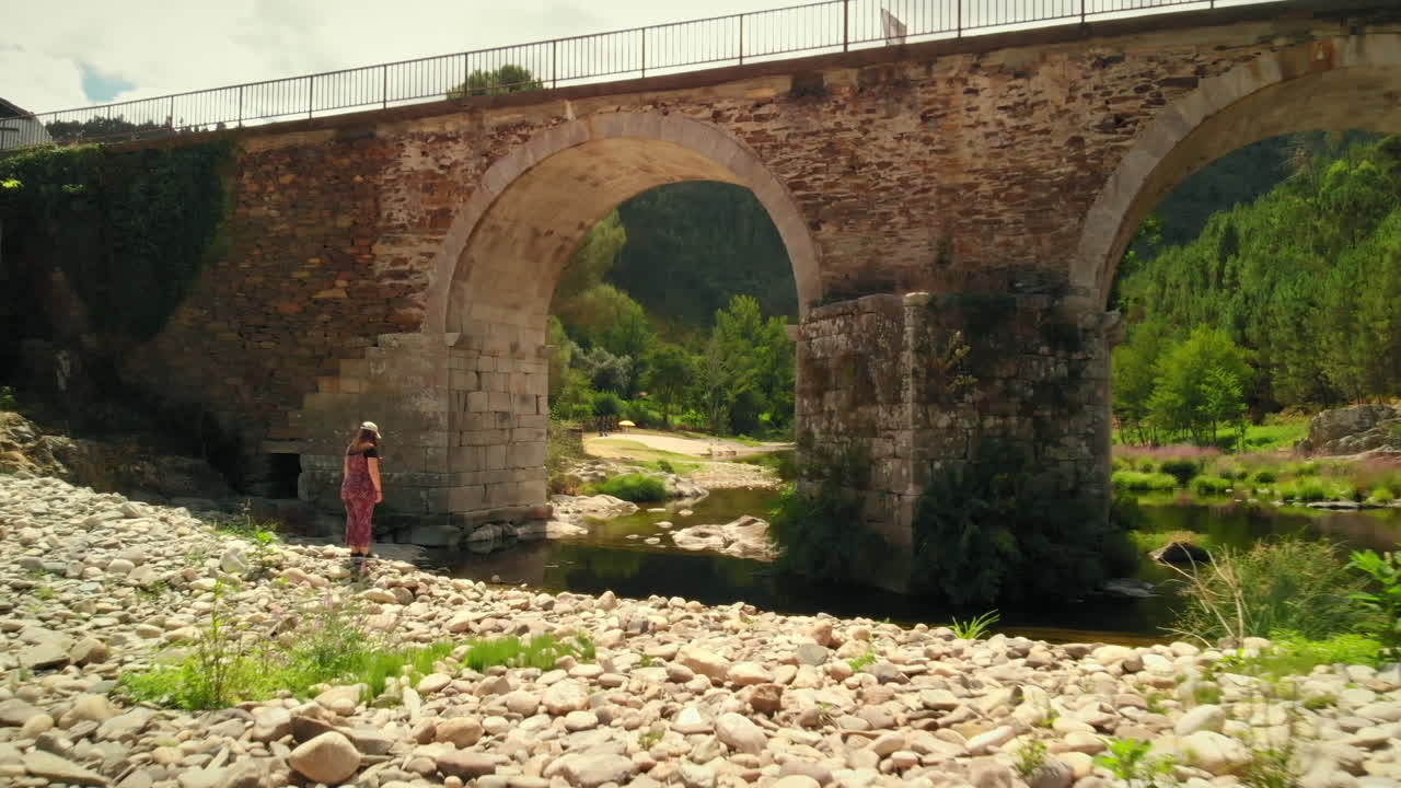 Girl by the River with a Stone Bridge in a Summer Day