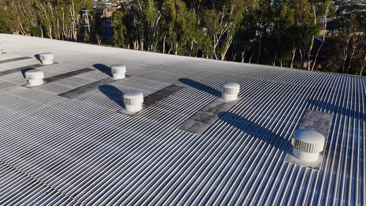 Aerial footage of a metal roof with ventilation units, captured in clear daylight over Gold Coast, Australia