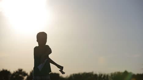 Kid Playing With Flying Paper Plane. Cute boy throwing a paper airplane into the sky in grass