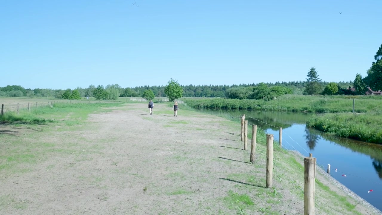 Two People Walking Along a Riverbank in the Countryside