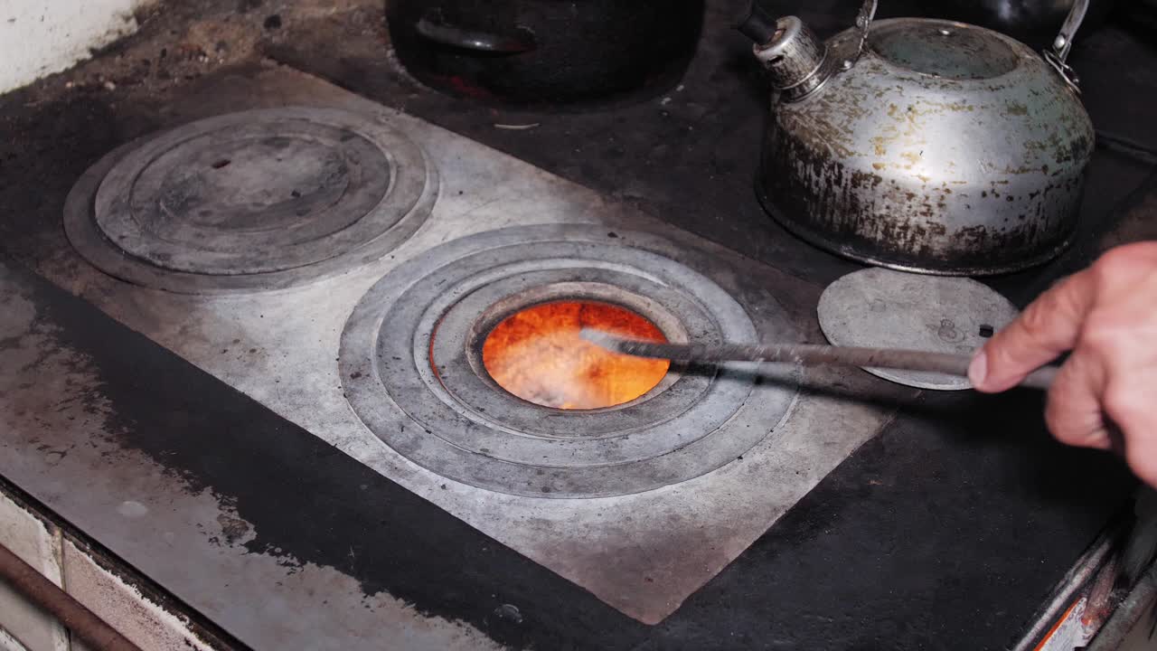 남자는 더러운 주전자를 집어 들고, 포커로 벽난로를 옮기고, 소박한 오래된 부엌 난로의 난로에 있는 통나무를 곧게 만듭니다