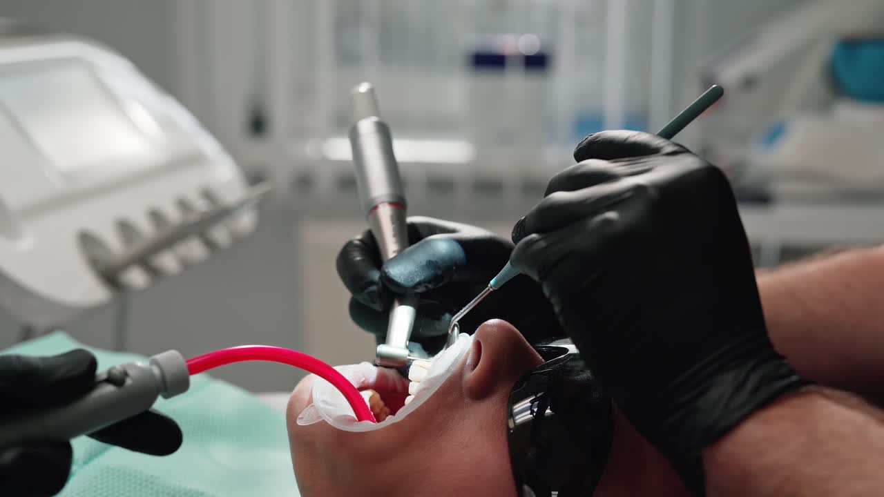 Face of a patient in protective glasses at dentist's visit. Stomatologist together with a nurse working with dental tools during teeth treatment. Close-up.