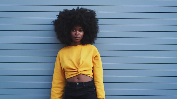 Young black woman with afro turns and smiles to camera, crosses arms and looks away, close up